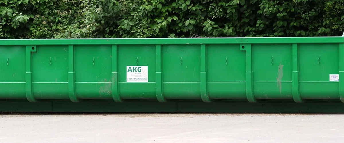 Benne verte vide stationnée devant une haie, prête à recevoir des déchets verts