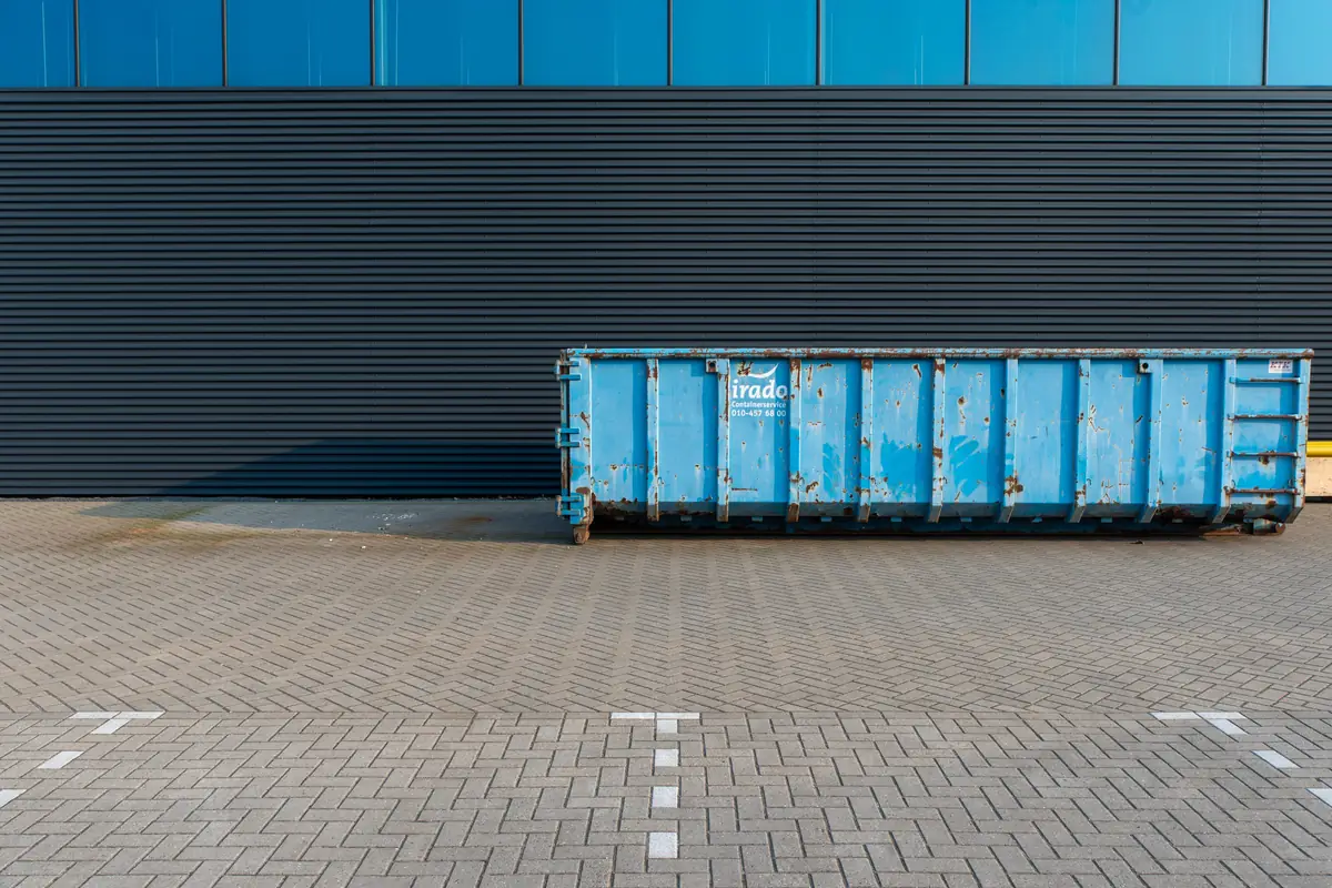 Benne métallique bleue posée sur une aire pavée le long d'un bâtiment