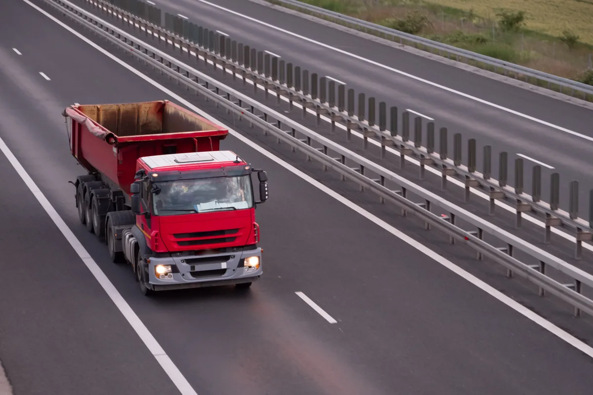 Camion benne rouge circulant sur une route à deux voies, vu de dessus
