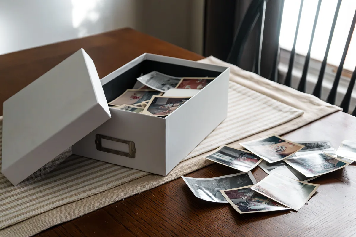 Boîte d'archives ouverte contenant des photographies de famille, posée près d'une fenêtre