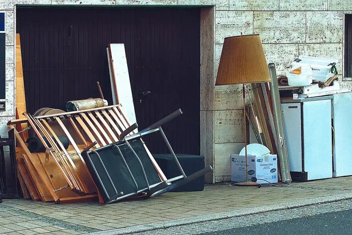 Encombrants déposés devant un garage : lampadaire, sommier, réfrigérateur et planches