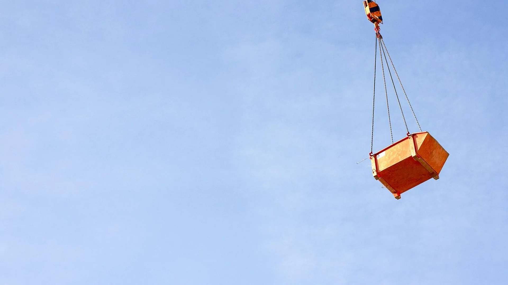Benne orange soulevée par une grue au-dessus d'un chantier, sous un ciel dégagé